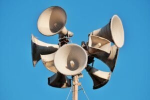 Close-up of multiple aged megaphones on a pole against a clear blue sky.