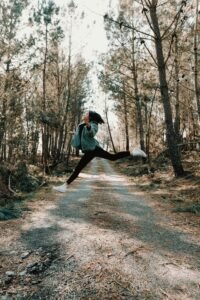 Woman jumping mid-air on a forest pathway in autumn, surrounded by trees.