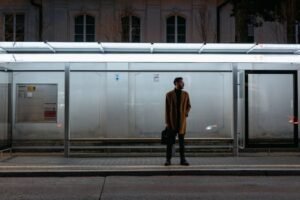 Man in coat waiting at an empty bus stop at night, urban scene.