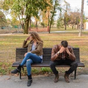 An upset couple seated on a park bench, expressing frustration during an autumn day.