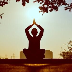 Silhouette of a person practicing yoga outdoors during sunrise, creating a calming atmosphere.