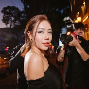 A glamorous woman in black poses confidently for photographers at a night event.