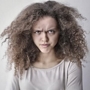 Portrait of a woman with curly hair showing an angry facial expression. Ideal for emotion-based content.
