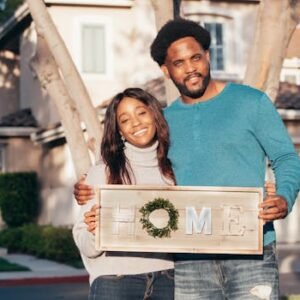 Happy couple holding a 'Home' sign in front of their new house, symbolizing joy and togetherness.